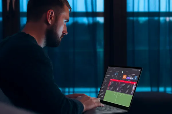 GOOD111 মোবাইল অ্যাপ — ক্যাসিনো ও স্পোর্টসের সম্পূর্ণ হাব একজন পুরুষ তার ল্যাপটপে মনোযোগ দিয়ে কাজ করছেন, ব্যাকগ্রাউন্ডে লাইভ স্ট্যাটস — যা GOOD111 মোবাইল অ্যাপের স্পোর্টস ও গেমিং ফিচারগুলোকে তুলে ধরে।