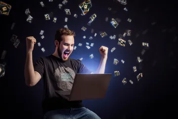 A man celebrating a winning moment on his laptop while gaming symbols float around him, capturing the excitement of GOOD111 games.